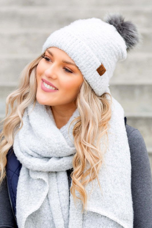 White bouclé knit hat with faux fur pom worn with scarf, angled view