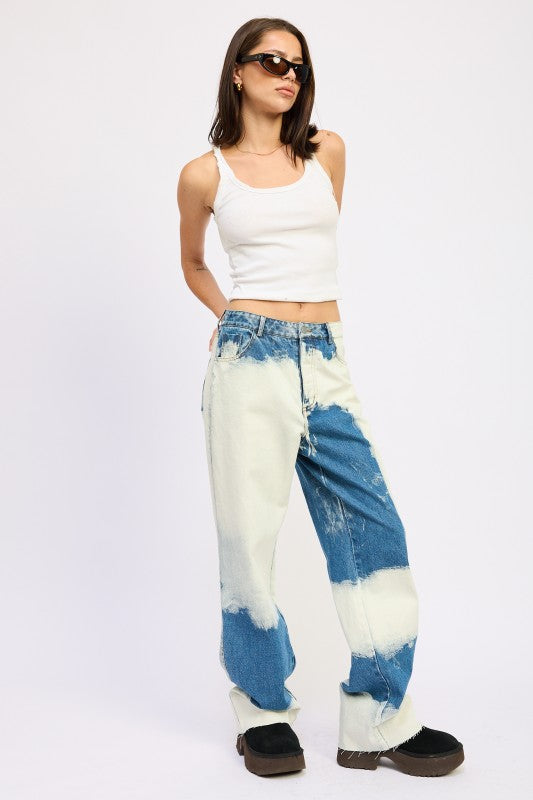 Angled view of AVAH tie-dye washed denim jeans styled with tank, platform shoes, and sunglasses