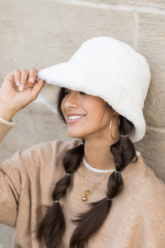 Side view of white faux-fur bucket hat styled with beige sweater