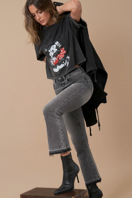 Woman wearing a black graphic t-shirt, gray jeans, and black boots on a beige background