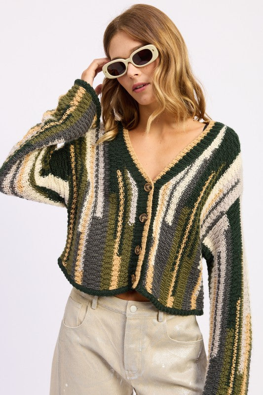 Model wearing a olive patterned cardigan and sunglasses on a white background