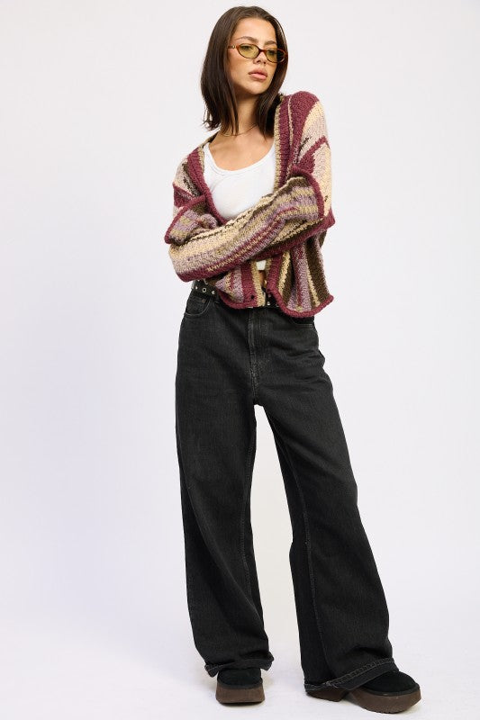 Model wearing a patterned cardigan and black jeans on a white background