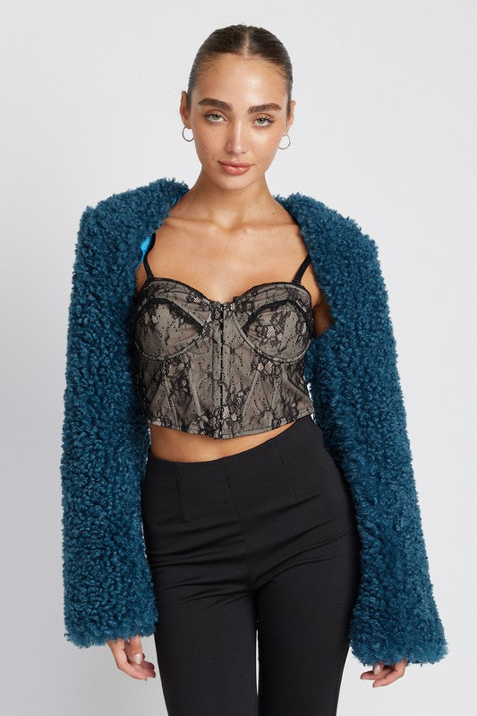 Model wearing cropped plush shrug layered over lace top and black pants, front view