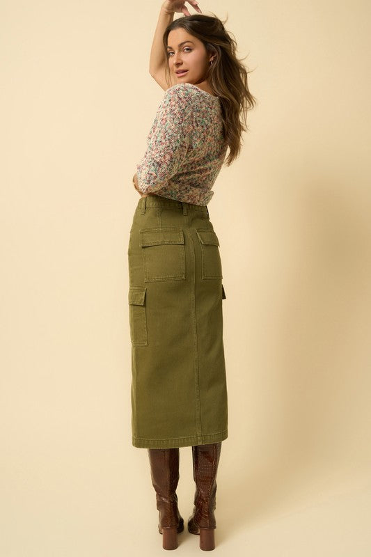 Model turning slightly to show rear fit of olive cargo denim skirt.
