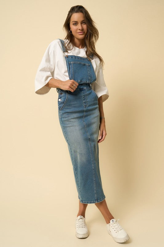 Model wearing denim overall midi dress with white tee and sneakers – front view