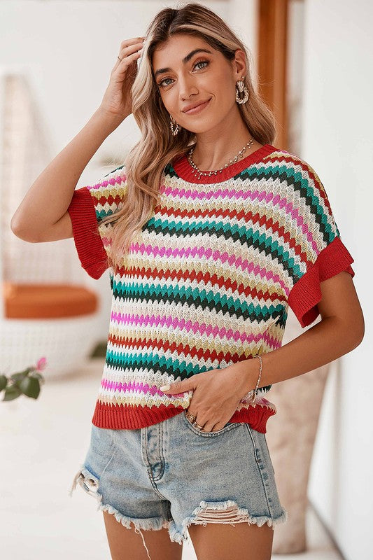 Model wearing colorful zigzag knit top with red trim, posing indoors with hand in hair-AVAH