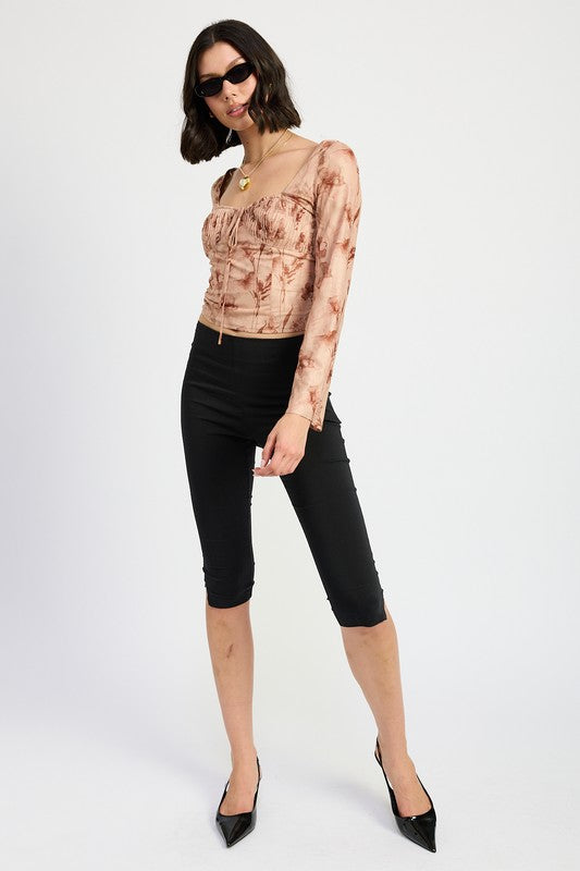 Angled view of model wearing brown floral top with sunglasses and black pants