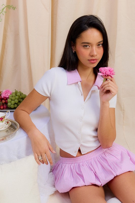 AVAH-Model wearing white cropped polo top with pink collar, seated at floral picnic setup