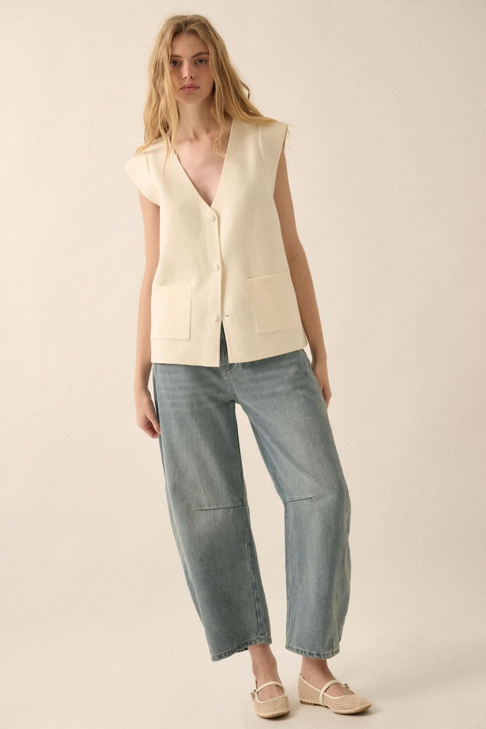 Model standing front-facing in studio, styled with wide-leg barrel jeans and cream sleeveless cardigan vest.