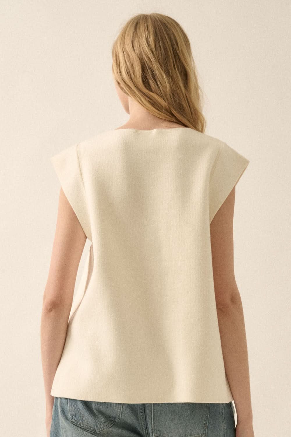Back view of cream sleeveless cardigan vest, styled with loose denim.