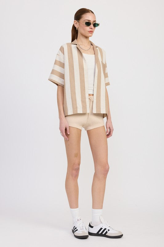 Angled view of model in mocha striped oversized top paired with neutral ribbed shorts, sneakers, and sunglasses