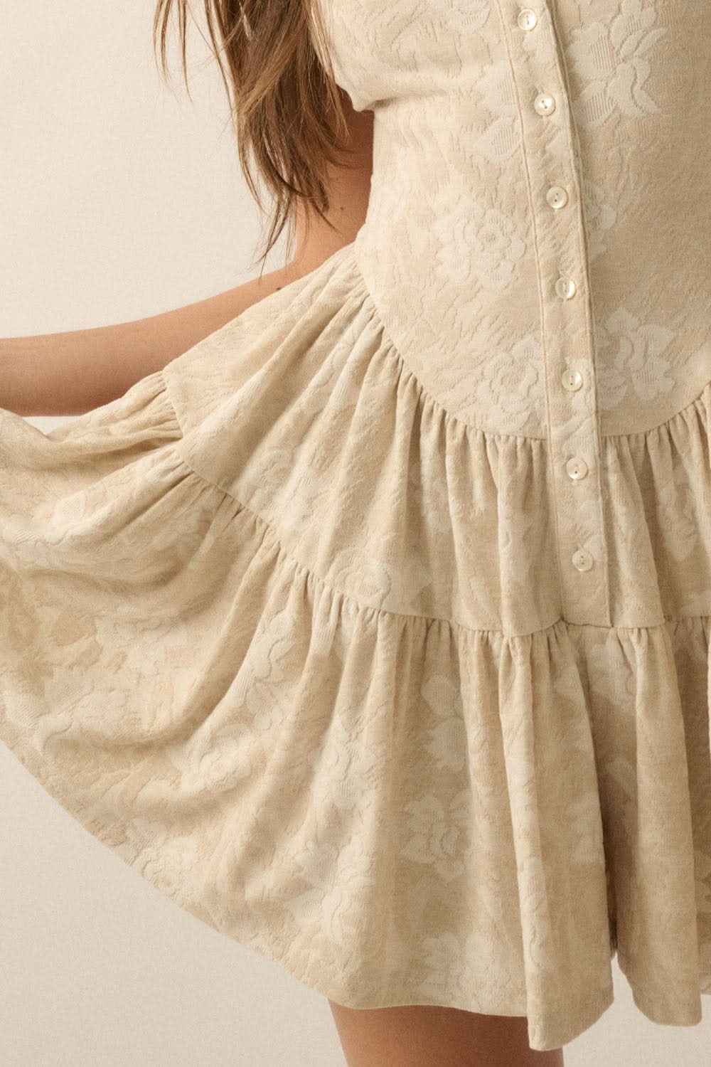 Close-up of tiered ruffle shorts in oatmeal jacquard fabric with pearlesque button detailing.