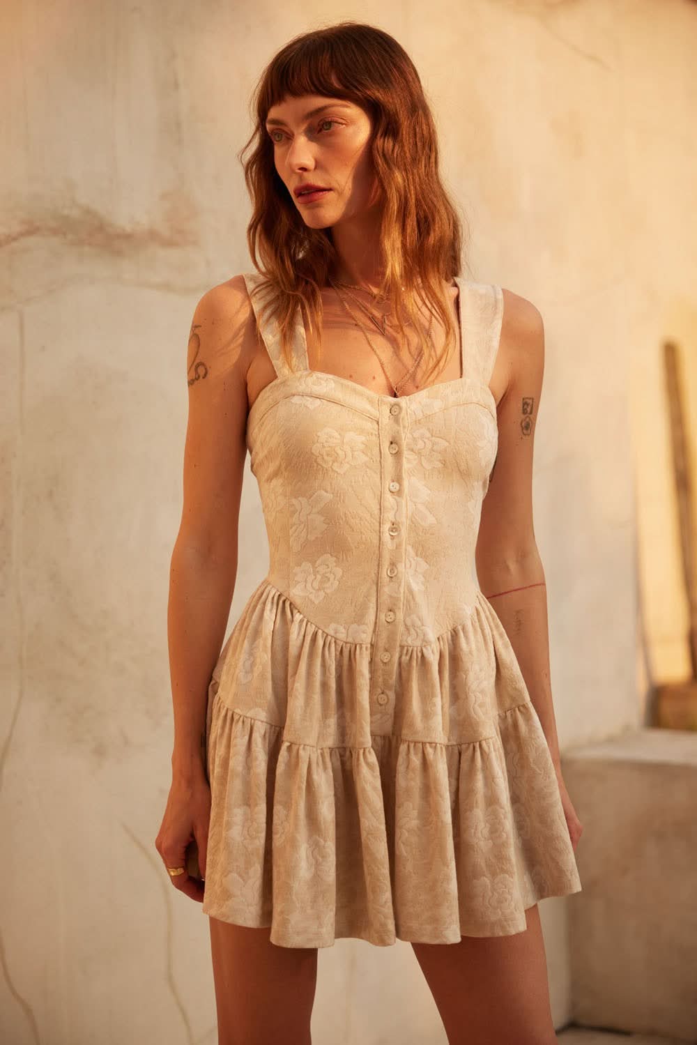 AVAH-Model wearing oatmeal floral jacquard romper with sweetheart neckline and ruffled shorts, standing in warm sunset light.