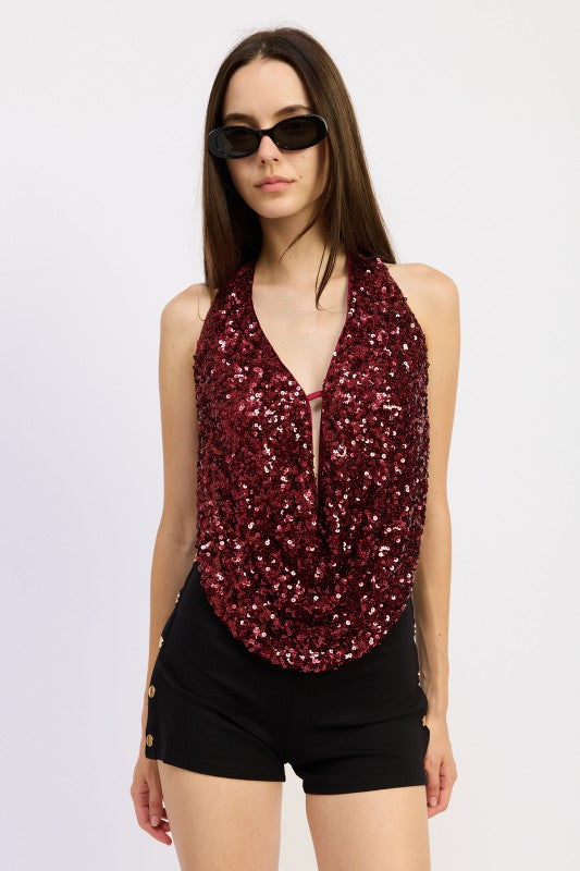 Model wearing a red sequin draped halter top with deep neckline, paired with black shorts and sunglasses.