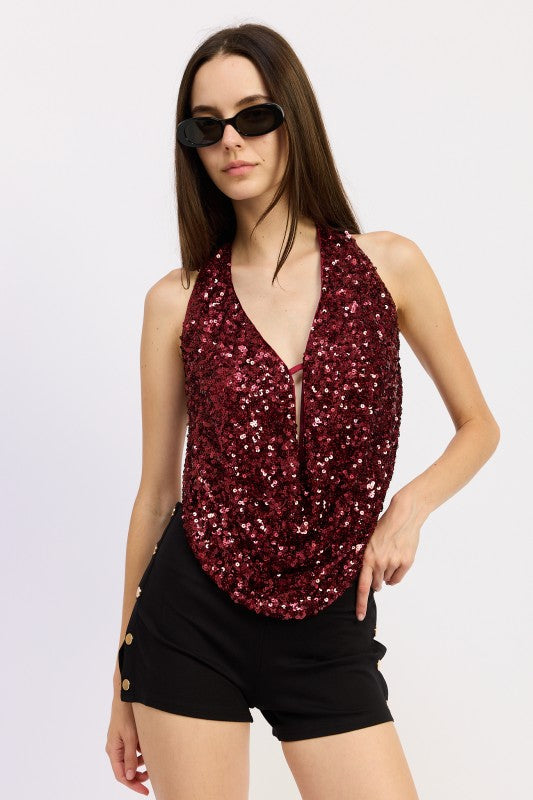 Model wearing a red sequin draped halter top with deep neckline, paired with black shorts and sunglasses.