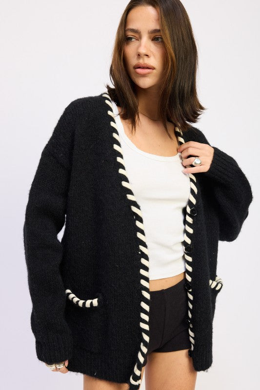 Model posing in black cardigan with white contrast edge — angled front view.