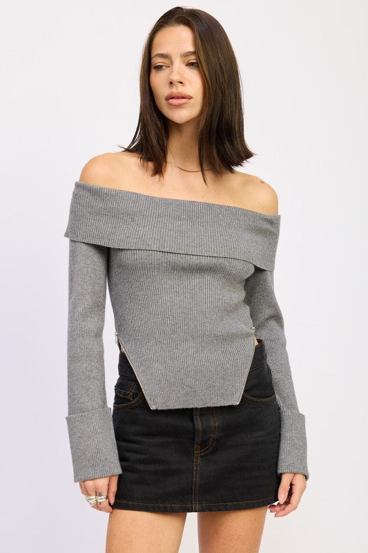 Model wearing a grey off the shoulder ribbed sweater with foldover neckline and pointed hem, front view