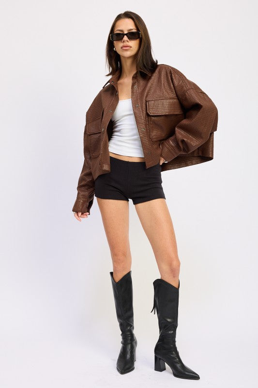 Model styled in AVAH cropped faux leather jacket with grid embossing, paired with black shorts, white tank, and tall black boots.