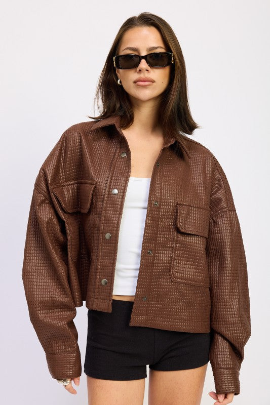 Model wearing AVAH brown cropped jacket with grid texture, collared neckline, and oversized fit styled with a white tank and black shorts.
