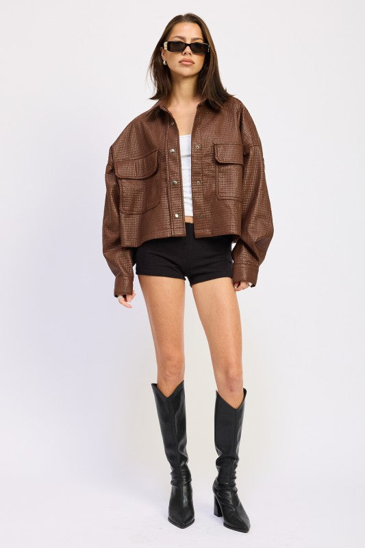 Model styled in AVAH brown cropped jacket with grid embossing, paired with black shorts, white tank, and tall black boots.