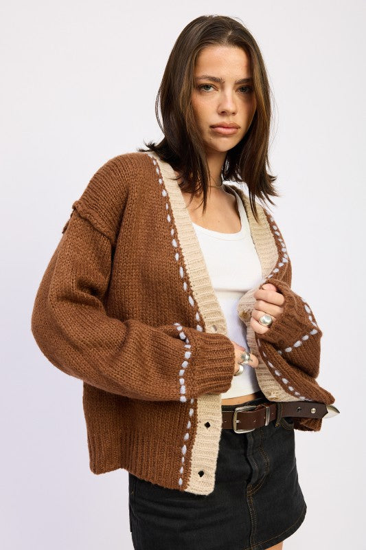 Side angle of brown knit cardigan with beige trim and relaxed sleeves.