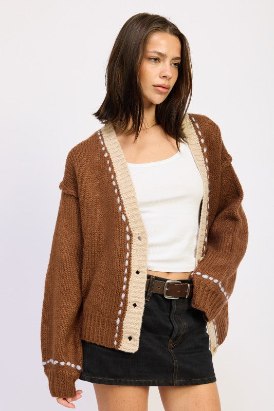 Side angle of brown knit cardigan with beige trim and relaxed sleeves.