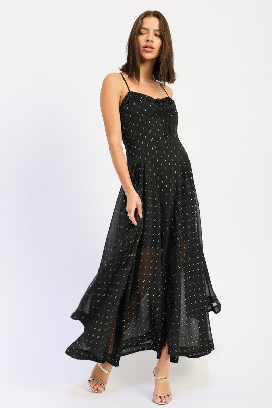 Black maxi dress with sheer dotted overlay and flowing A-line skirt, model holding hem to show movement