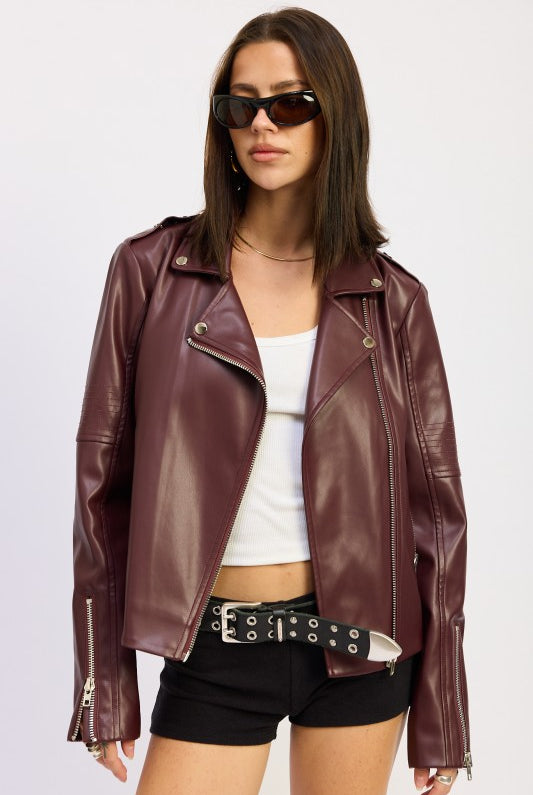 Model wearing burgundy faux leather moto jacket over white tank and black shorts.