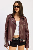 Model wearing burgundy faux leather moto jacket over white tank and black shorts.