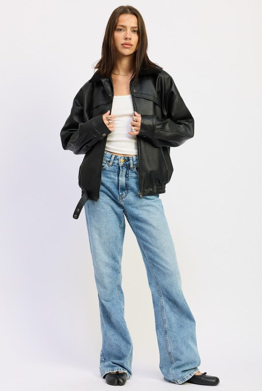 Model adjusting zipper of black vegan leather bomber jacket styled with denim jeans and white tank.