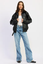 Model adjusting zipper of black vegan leather bomber jacket styled with denim jeans and white tank.