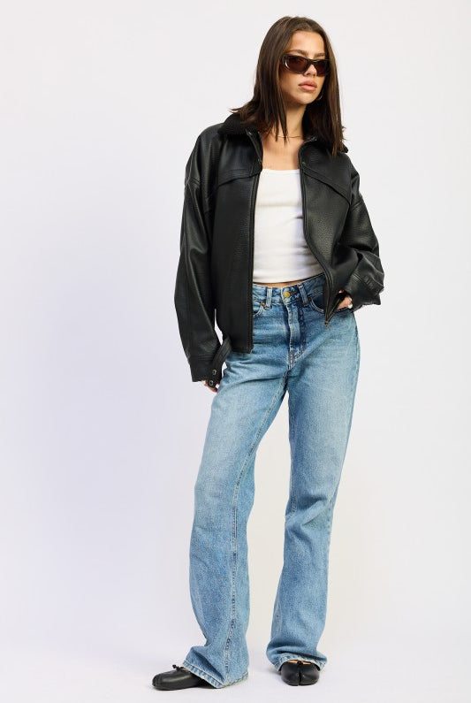 Full-body view of model wearing black vegan leather bomber jacket, white tank, and straight-leg light wash jeans.
