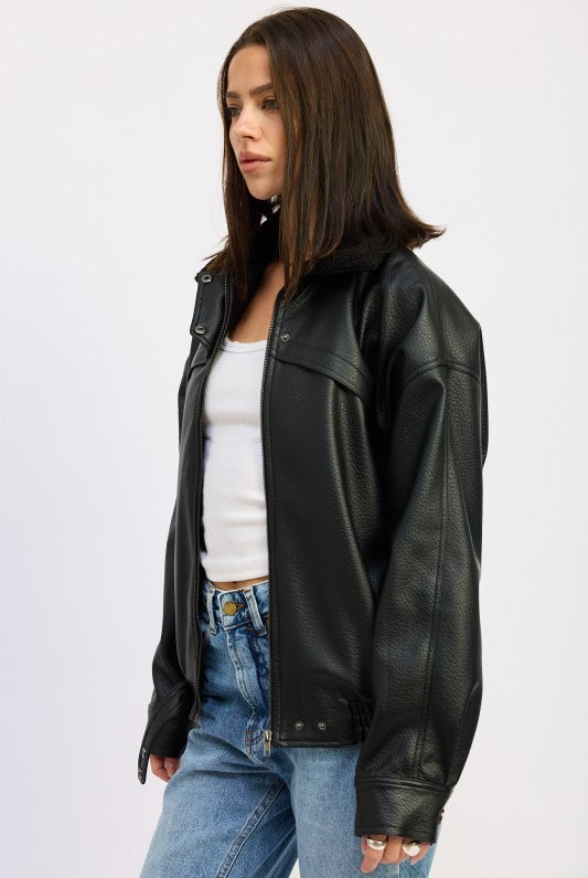 Side profile of model in black vegan leather bomber jacket paired with light blue jeans.