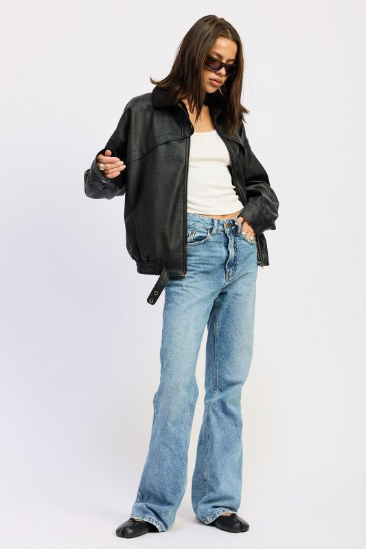 Full-body view of model wearing black vegan leather bomber jacket, white tank, and straight-leg light wash jeans.
