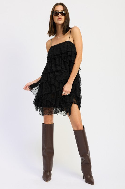 Model posing in black tiered lace mini dress with layered ruffles and boots.