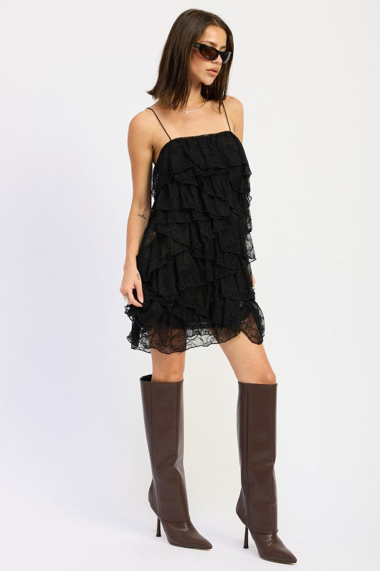 Angled view of black lace ruffle mini dress styled with knee-high boots.