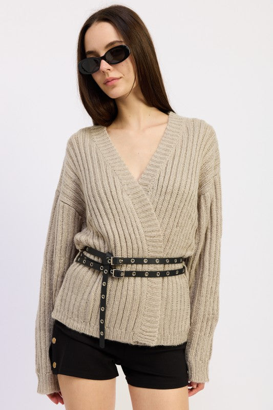 Model wearing warm grey ribbed wrap knit sweater with black grommet belt and black shorts – front view