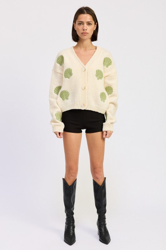Model in ivory seashell cardigan facing forward in black shorts and knee-high boots.