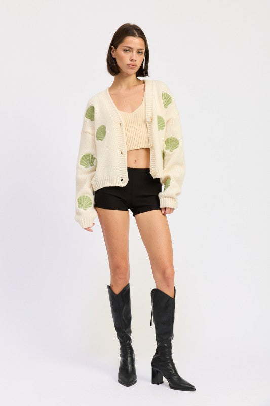 Model in ivory seashell cardigan facing forward in black shorts and knee-high boots.