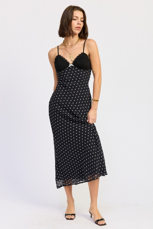 Model wearing black polka dot slip dress with lace bust, midi length, angled pose.