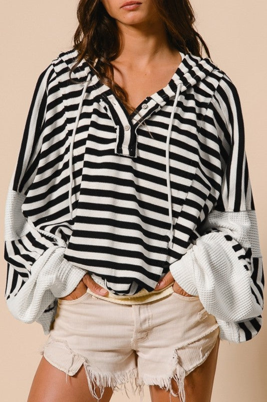 Close-up of striped hooded knit top showing button placket neckline, drawstrings, and contrast sleeve texture