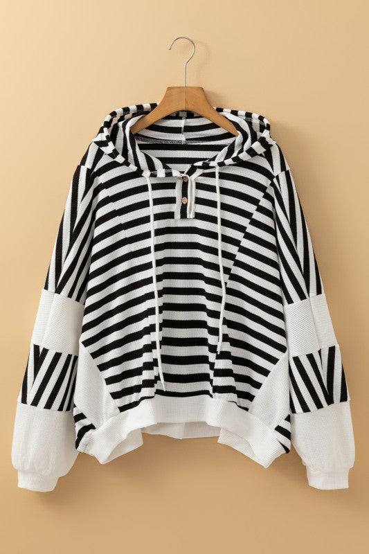 Black and white striped hooded pullover top on hanger with button neckline, drawstrings, and contrast sleeve panels