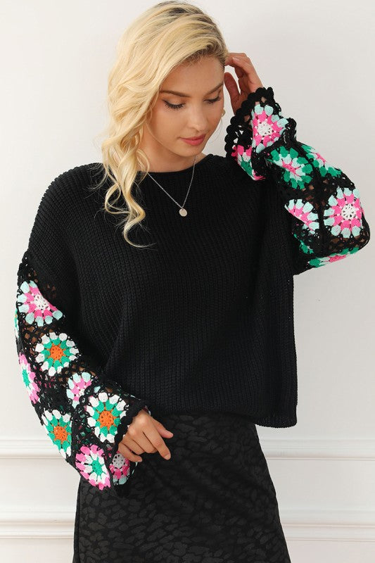 Detail view of multicolor crochet floral sleeve on black sweater