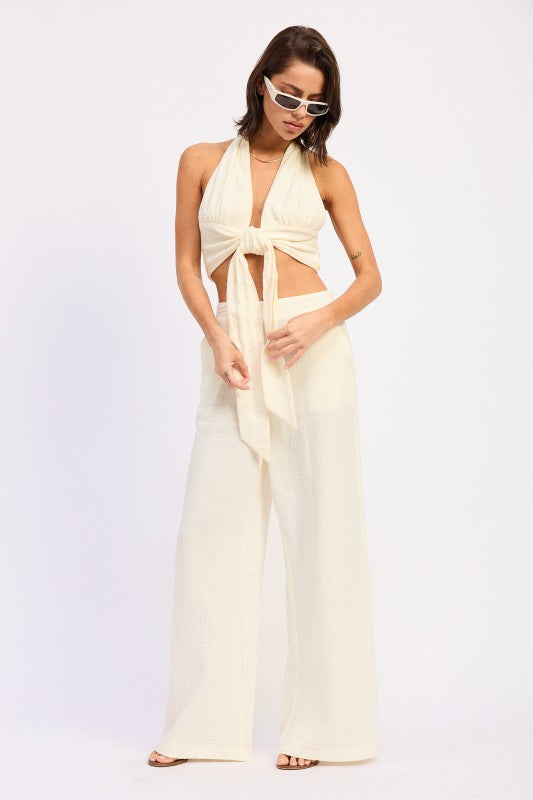 Model wearing ivory wide leg cotton gauze pants with elastic waist, styled with matching halter tie top