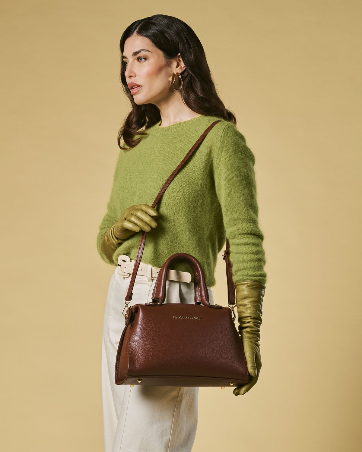 Woman holding a brown handbag against a beige background