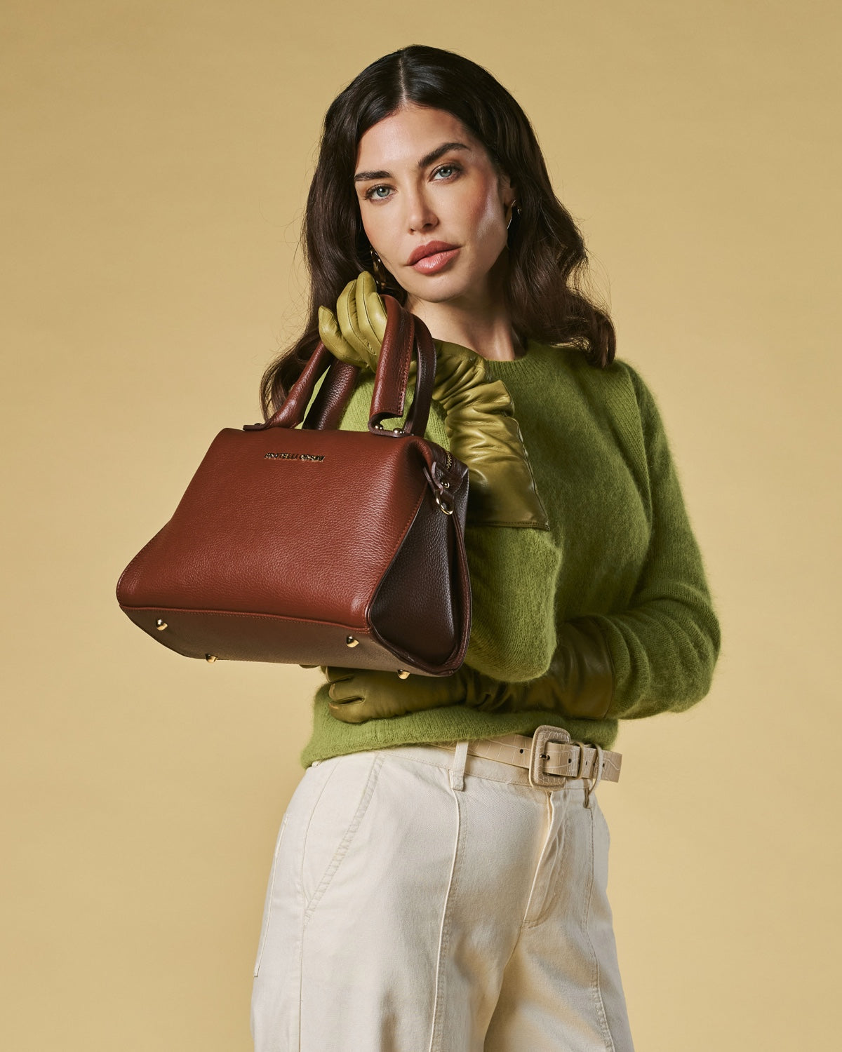 Woman holding a brown leather handbag against a beige background