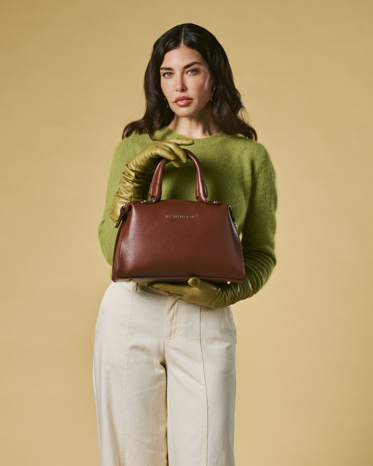 Woman holding a brown handbag against a beige background