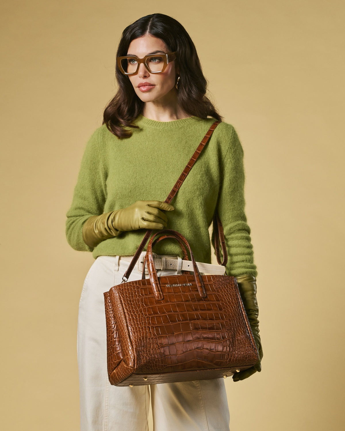 Woman in green sweater holding a brown handbag against a beige background