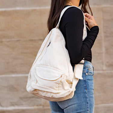 Person wearing a cream canvas single strap backpack against a beige wall