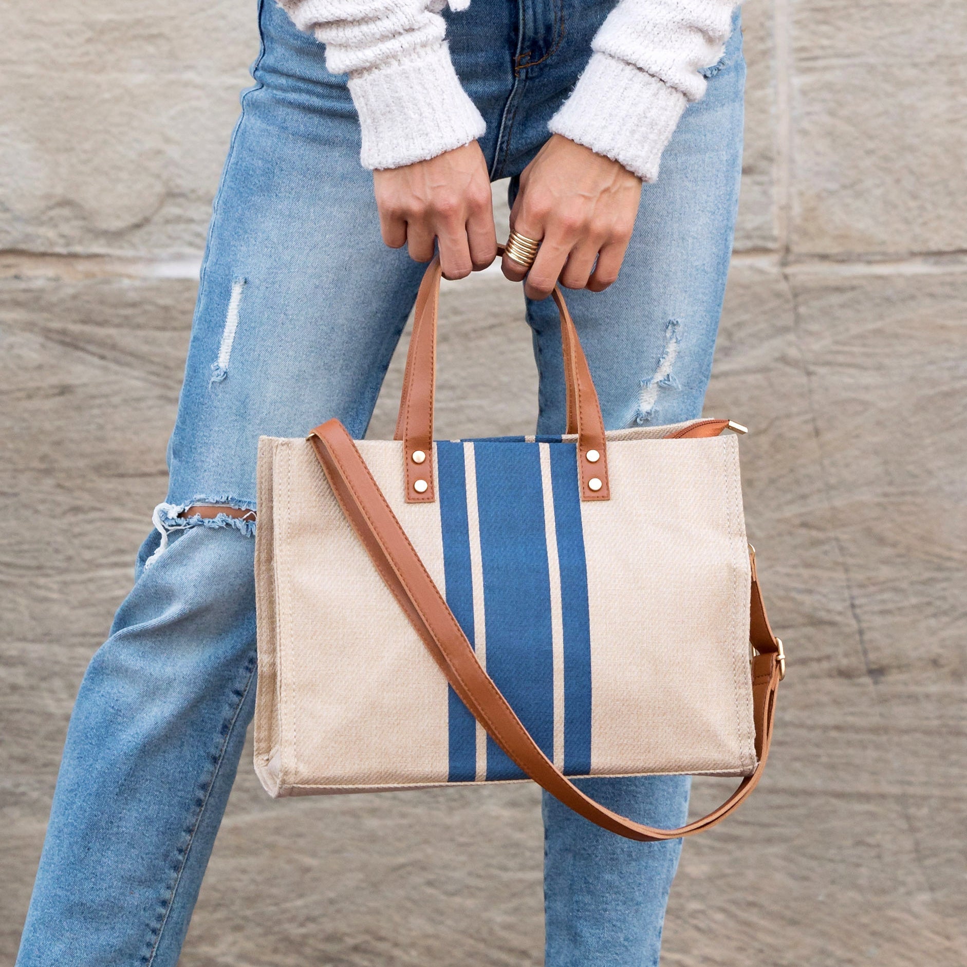 Person holding a striped tote bag with a brown strap against a wooden background